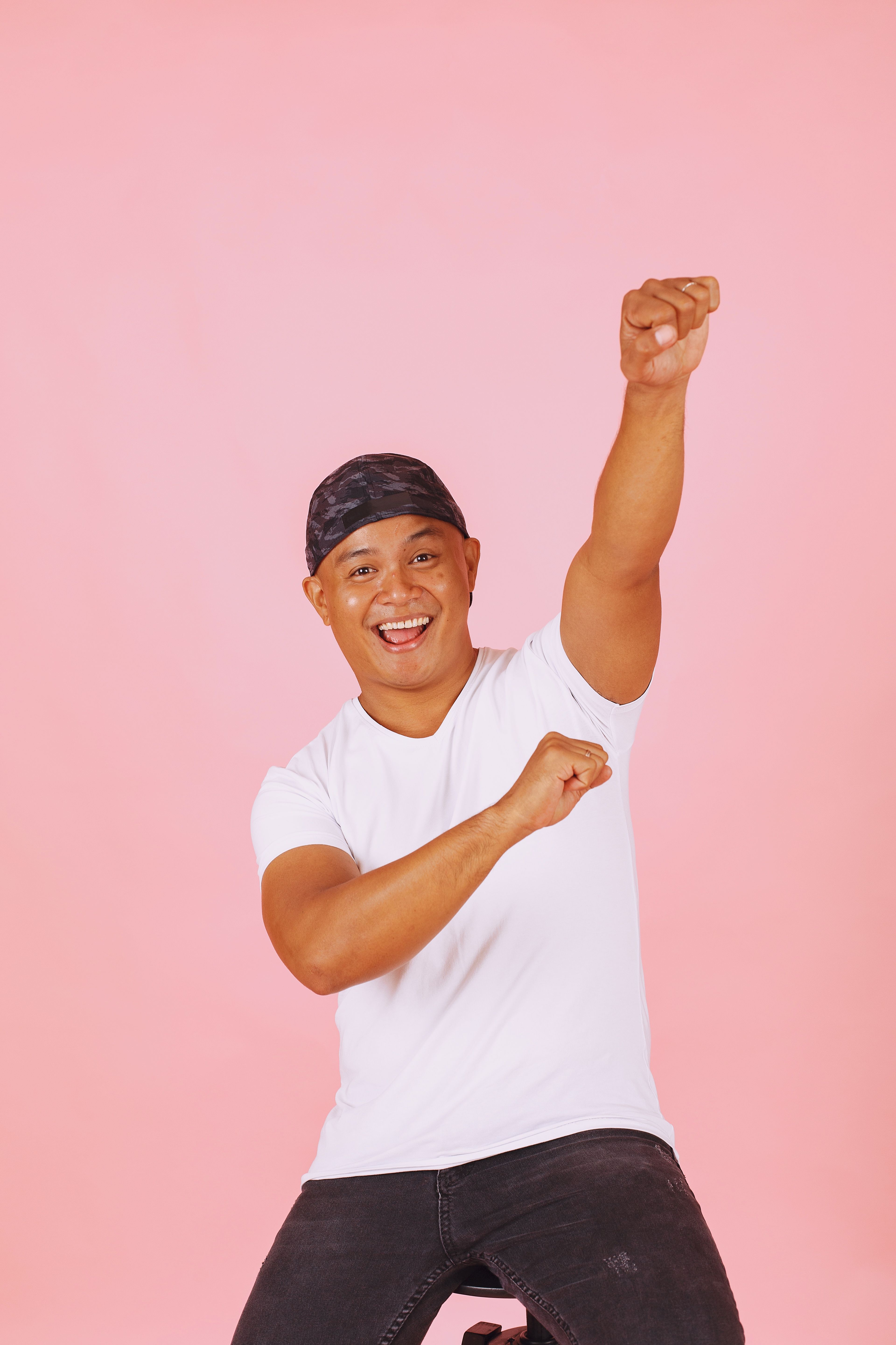 Happy young man in a white shirt celebrating with an energetic pose against a pink background.