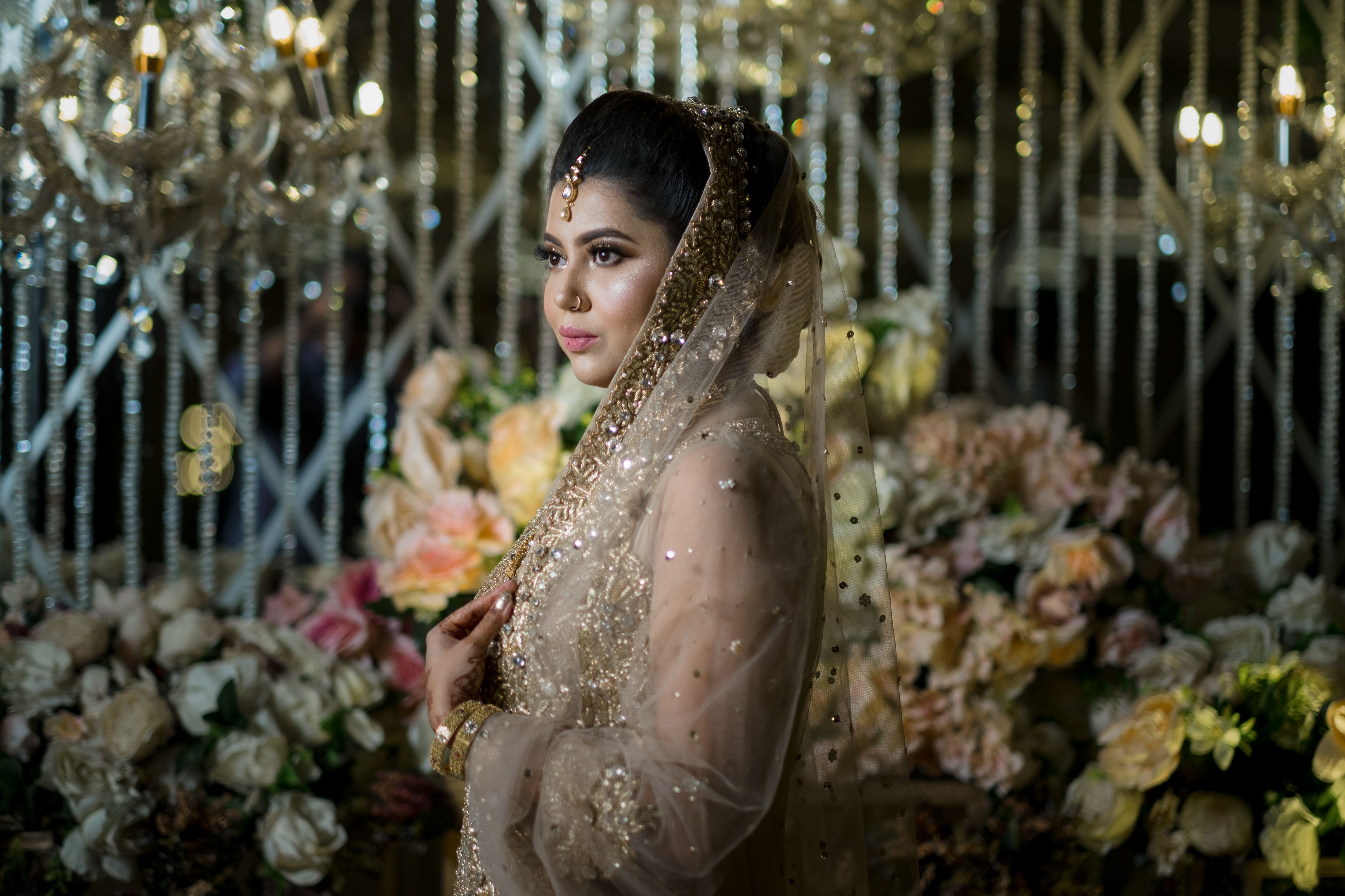 Elegant bride in a golden dress surrounded by floral arrangements and chandeliers.