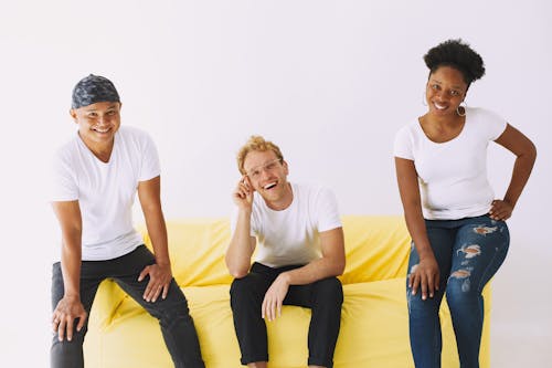 Free Three People in White Shirt Sitting on Sofa While Smiling at Camera Stock Photo