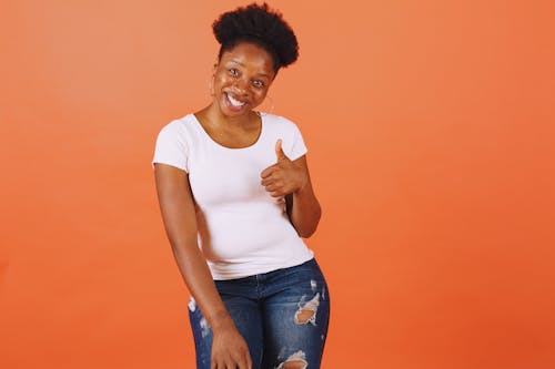 Woman in White Crew Neck T-shirt and Blue Denim Jeans Smiling at Camera