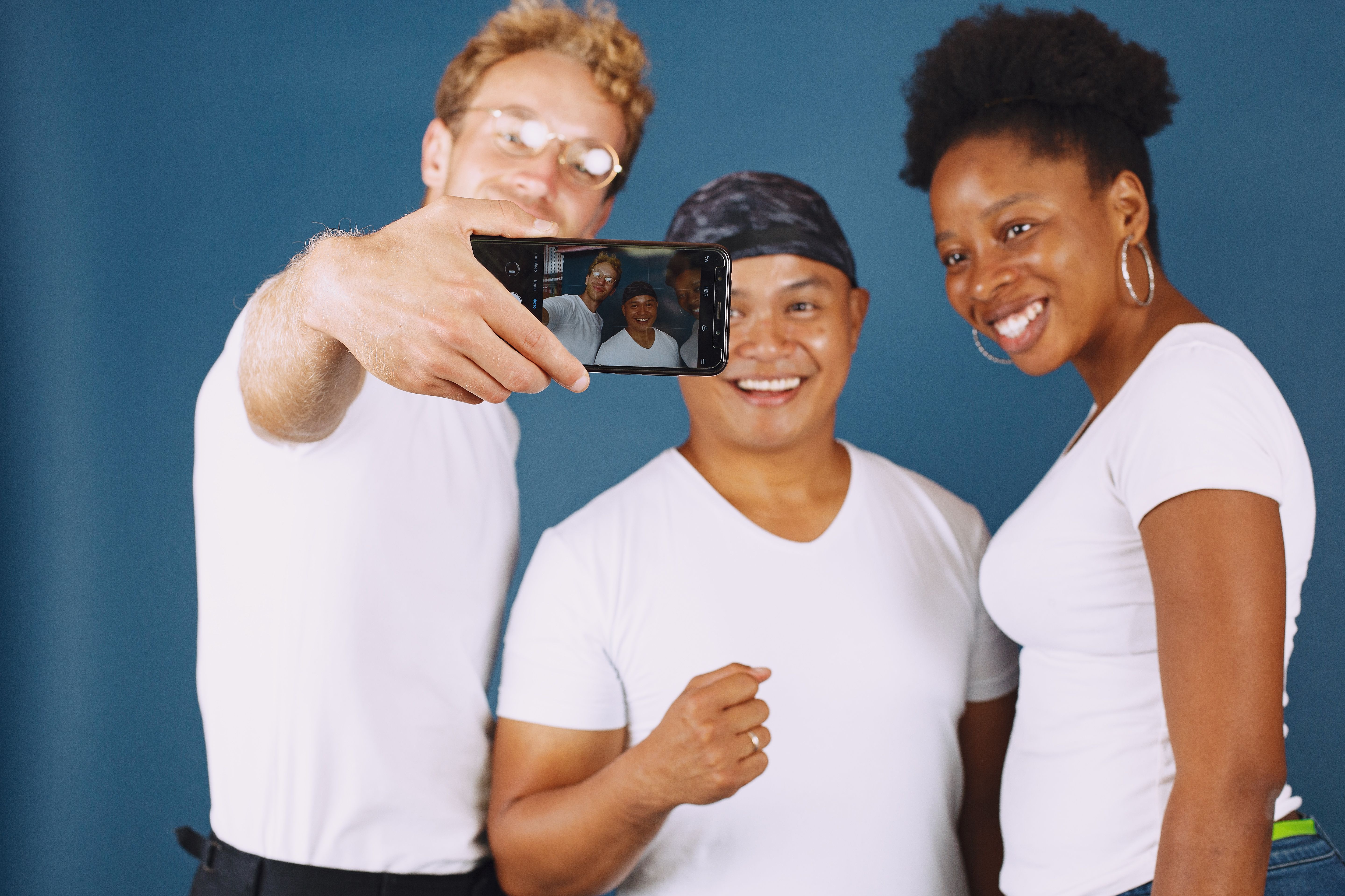 A diverse group of friends smiling and taking a selfie indoors.