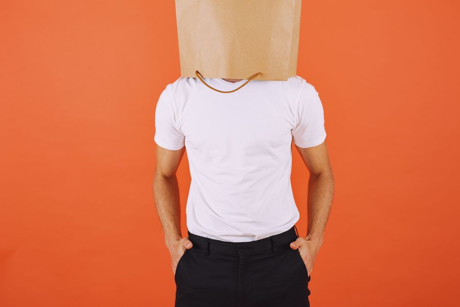 Man wearing a paper bag over his head poses against orange studio background. Man wearing a paper bag over his head poses against orange studio background.