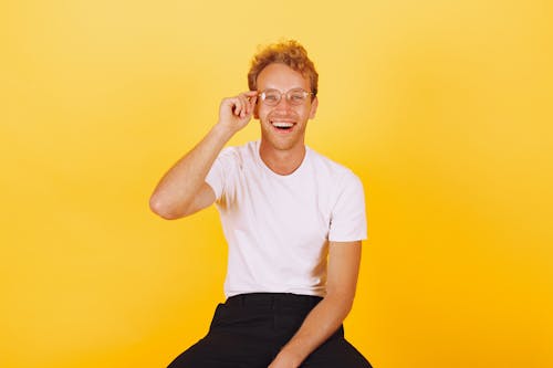 Free Smiling Man in White Crew Neck T-shirt and Black Pants Holding His Eyeglasses Stock Photo