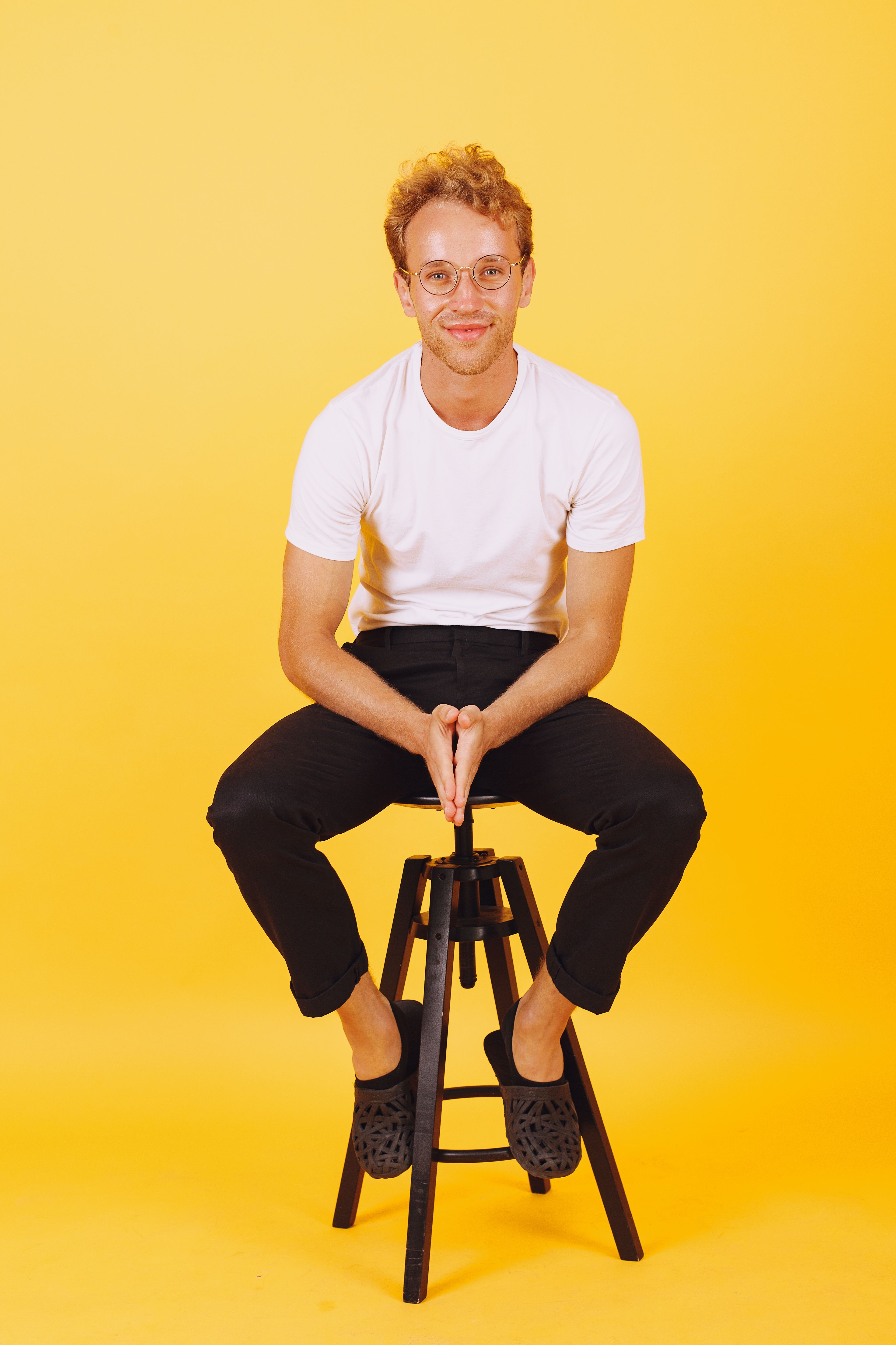 Caucasian man sitting on a stool in a studio with a vibrant yellow background.