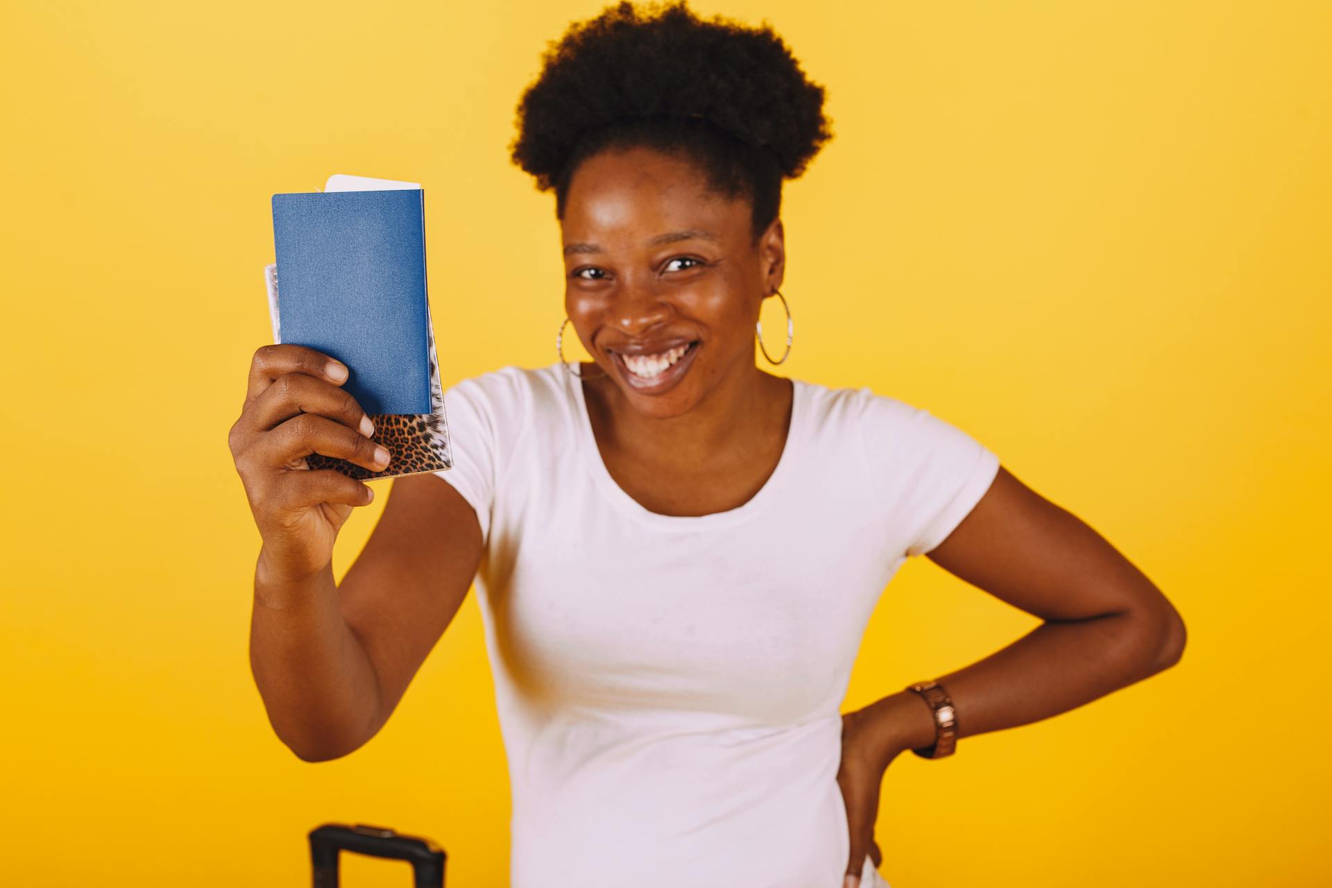 Smiling woman holding a passport, ready for a travel adventure against a yellow background.