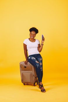 Smiling woman with luggage and passport preparing for a vacation on a yellow background.