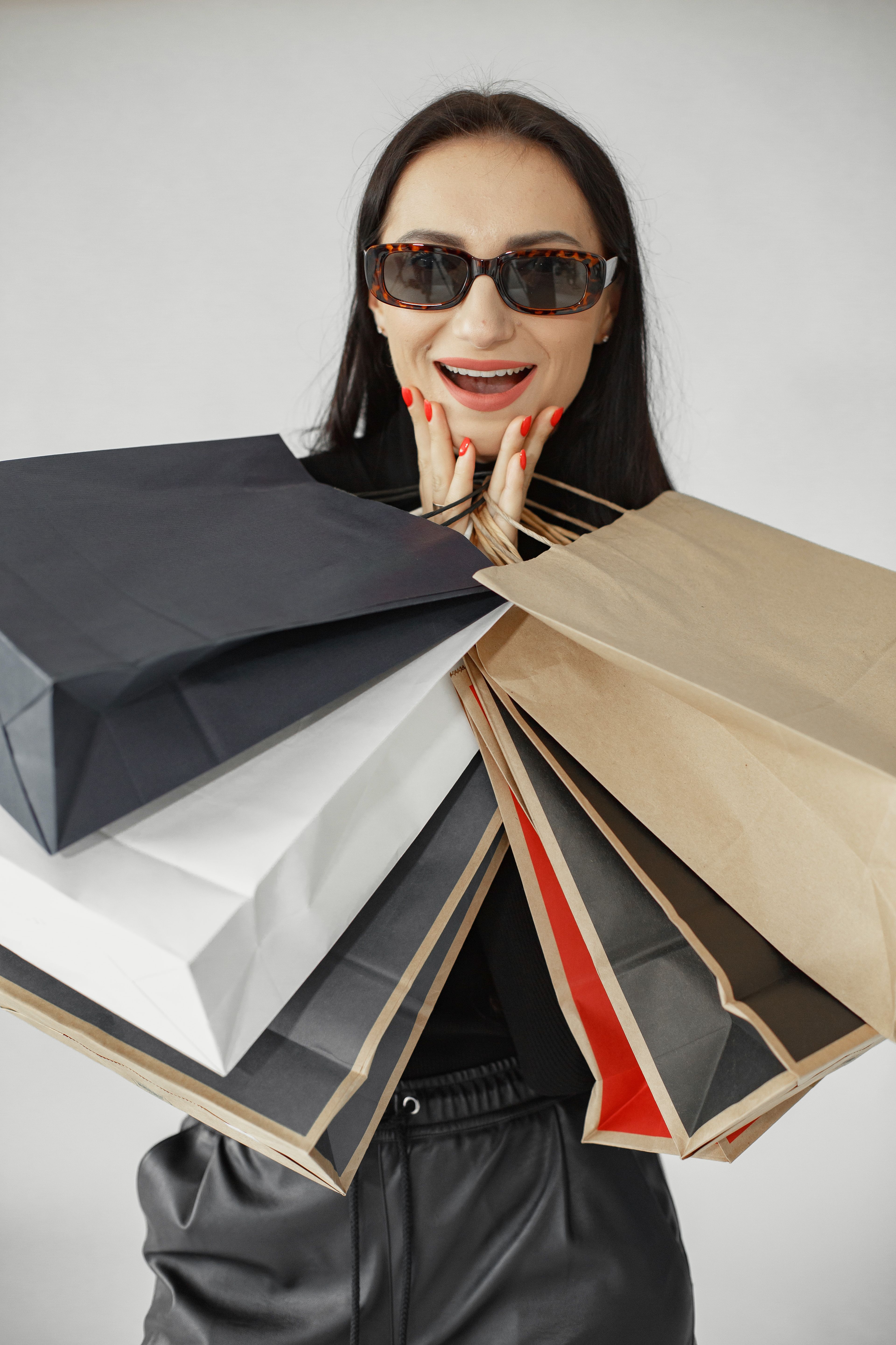 Fashionable woman with sunglasses excitedly holding multiple shopping bags indoors.
