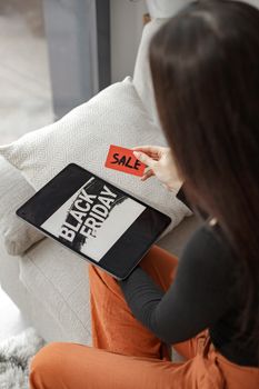 A woman holding a sale card while shopping on a digital tablet during Black Friday.