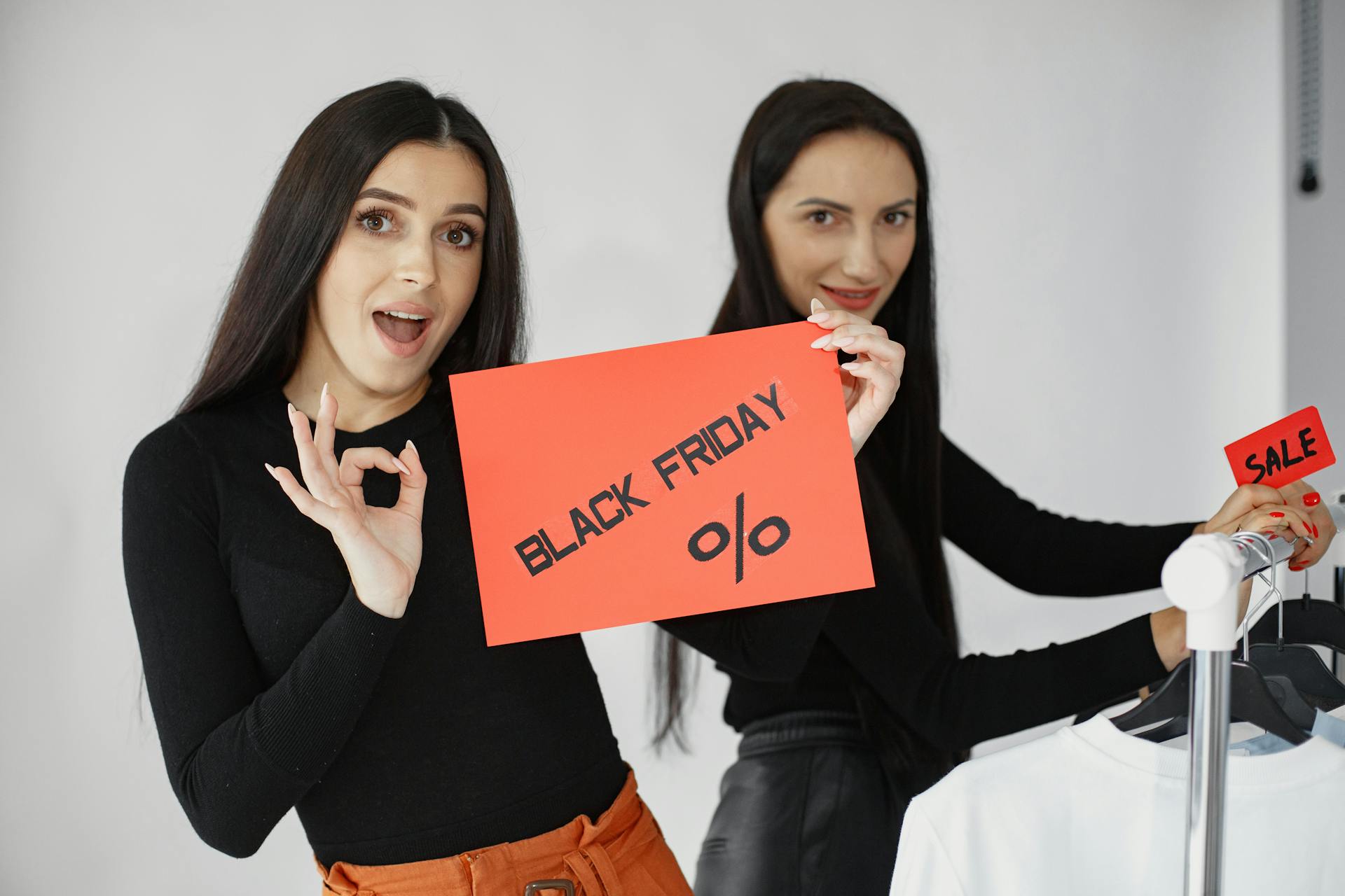 Two stylish women showcase Black Friday deals with enthusiasm in a studio setting.