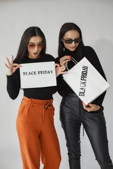 Two women showcasing Black Friday deals with stylish outfits and shopping bags.
