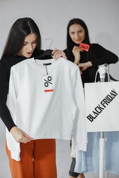 Woman holding a discount-tagged white shirt during Black Friday sale indoors.