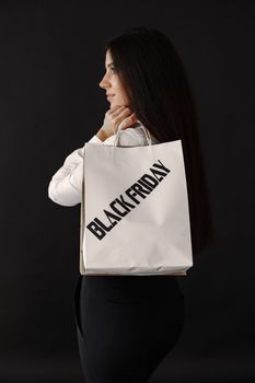 A fashionable woman holding a Black Friday shopping bag against a black background.