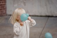 Anonymous blond kid in casual apparel playing with blue balloons on city street in daylight