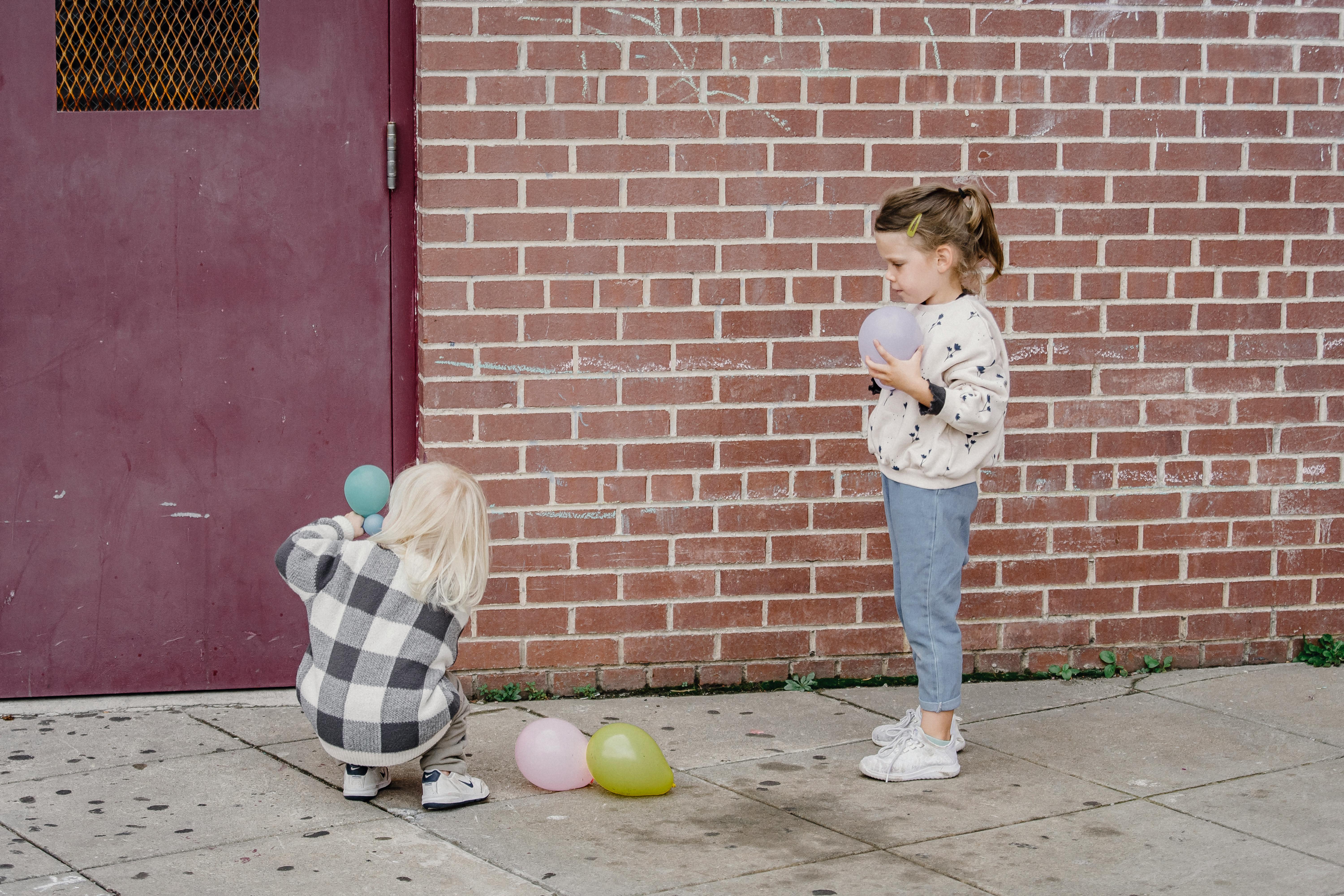 unrecognizable girlfriends playing with balloons near urban building
