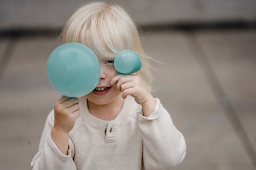 Smiling little girl covering face with balloons on street
