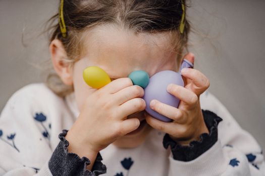 Crop anonymous shy kid in ornamental apparel with barrettes covering eyes with various balloons in daylight
