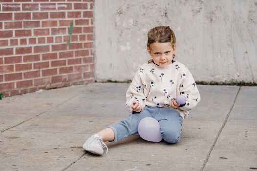Shy girl playing with balloons on urban pavement