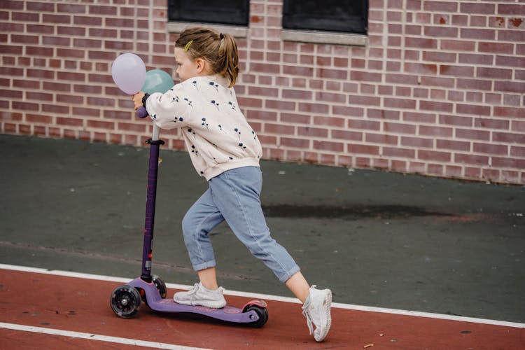 Girl With Balloons Riding Scooter On Sports Ground