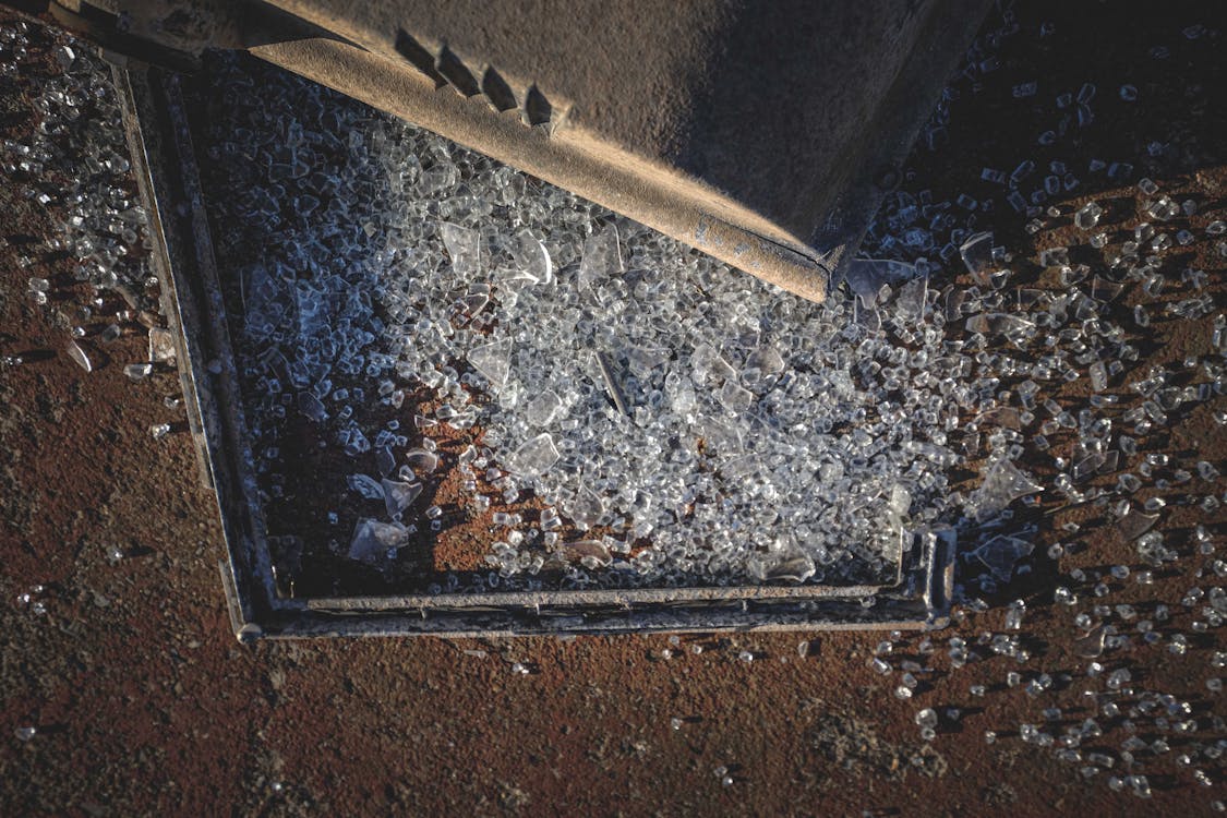 From above of pile of broken glass and metal frame scattered on rough ground on sunny day