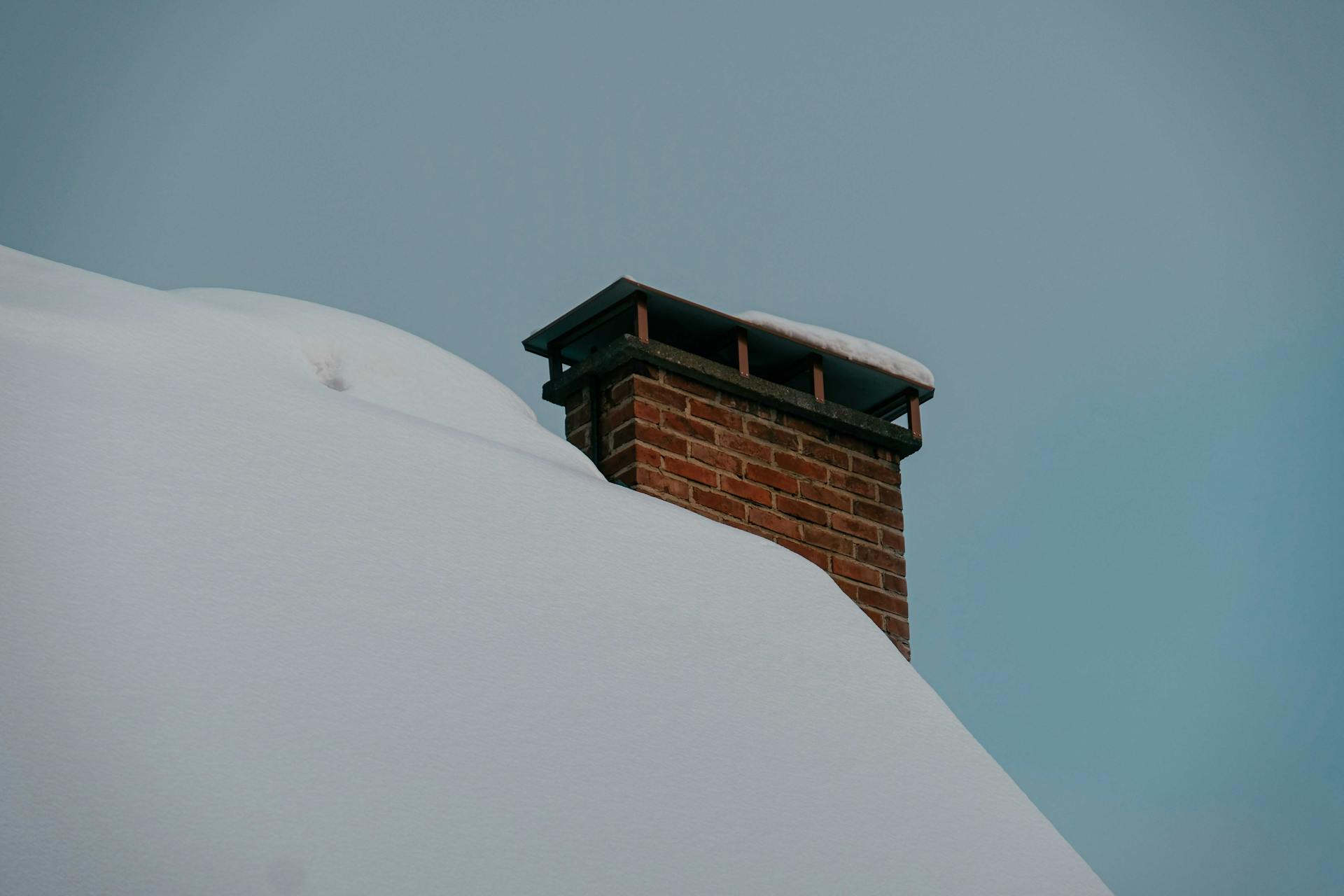 Roof of building with brick roof chimney covered with snow located against cloudless sky in winter time