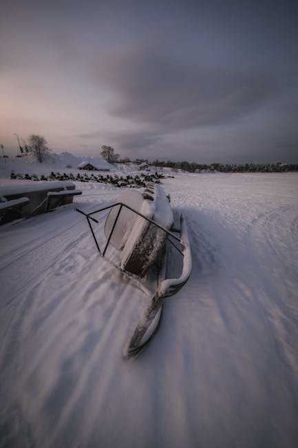 Forgotten snowmobile covered with hoarfrost and placed on side on snow in winter time  in field against cloudy sky