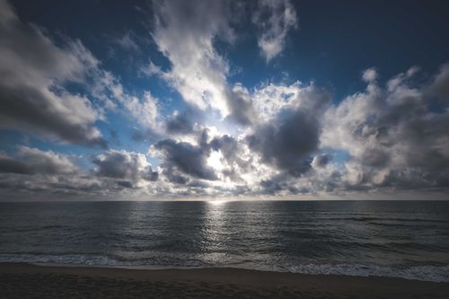 Free Picturesque seascape with rippling water washing sandy beach against cloudy sky with sun rays breaking through clouds in nature outside Stock Photo