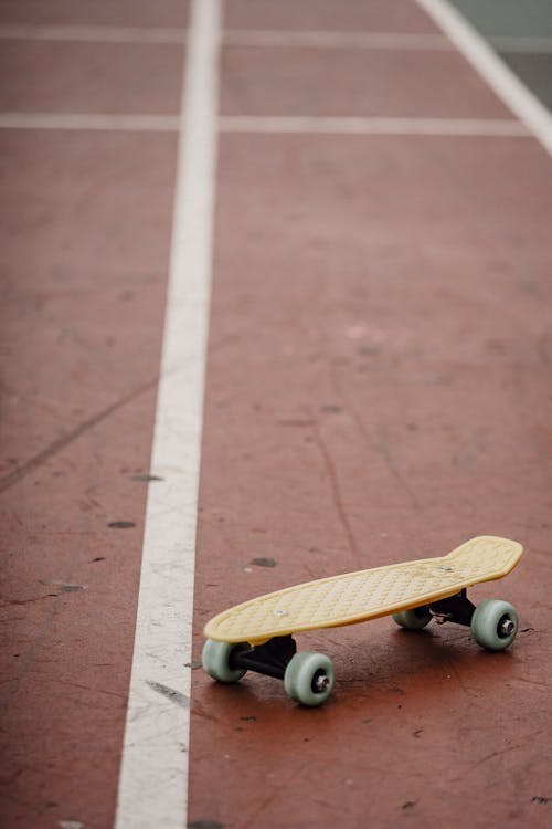 Modern yellow penny board with wheels placed on colorful sports ground with marked lines on street in city on blurred background