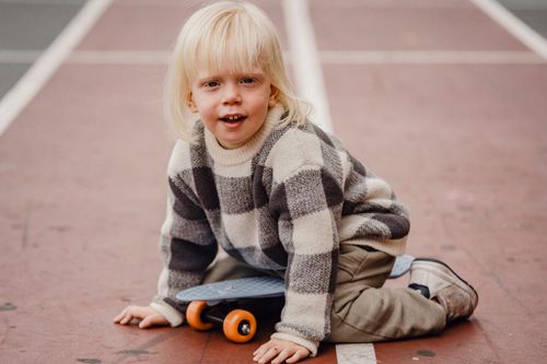 Free Full body of playful little kid looking at camera while sitting on sports ground with penny board against blurred background Stock Photo