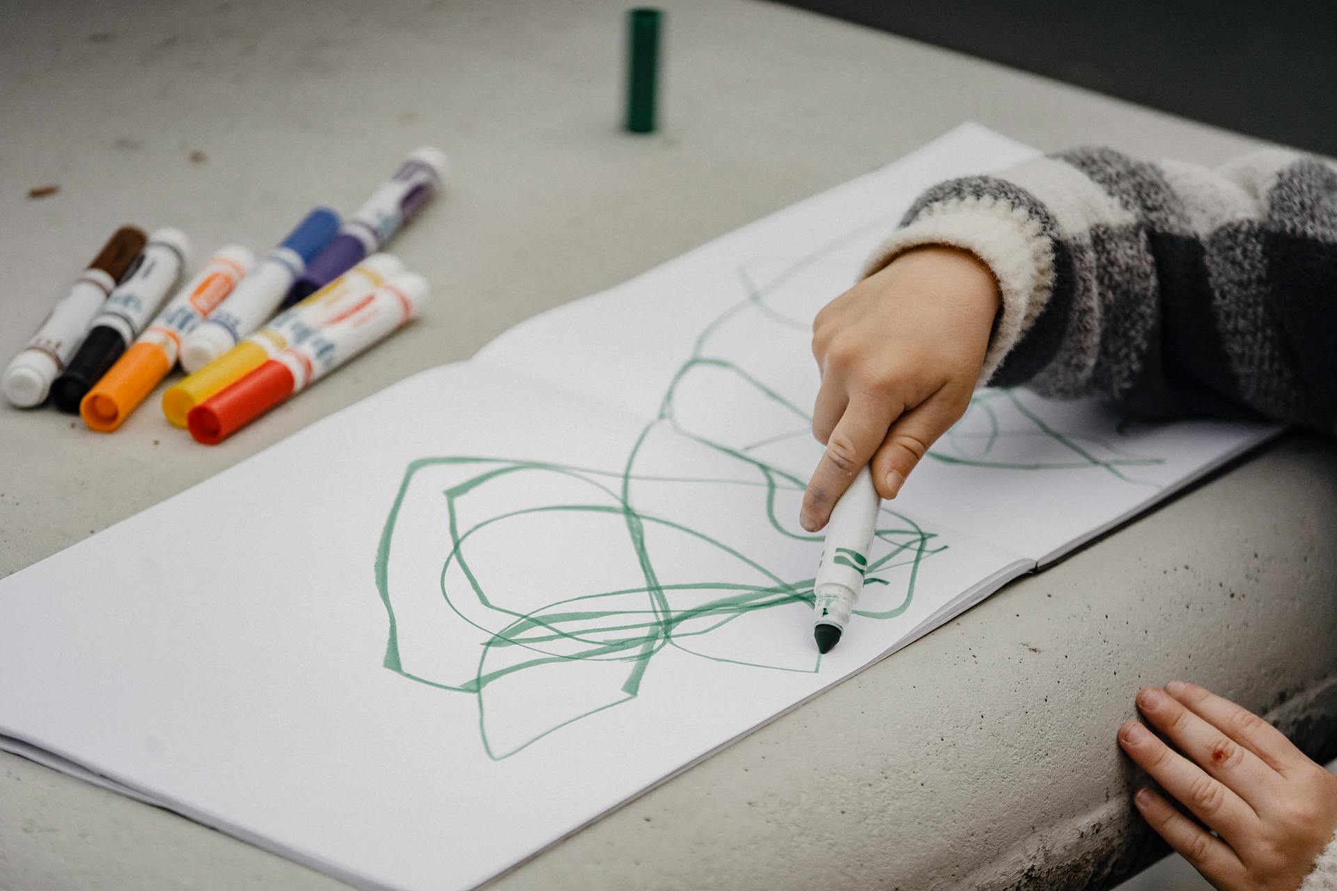 Crop kid drawing with marker at table