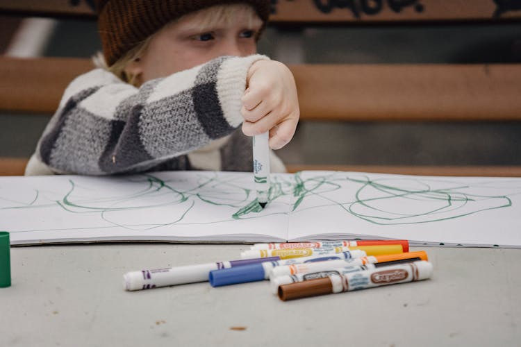 Child Drawing With Markers Sitting At Table On Playground