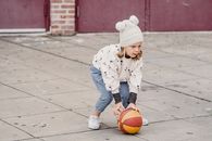 一个年幼的孩子穿着厚实的衣服，在寒冷的天气里于混凝土球场上玩篮球