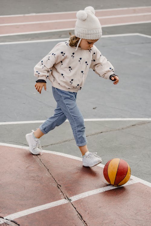 мальчик в сине белом свитере в горошек и синих джинсовых джинсах играет в баскетбол