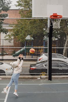 Side view full body of unrecognizable little kid throwing ball into hoop while playing game on sports ground on street