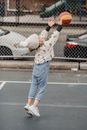 Side view full body of little kid jumping while throwing ball during game on sports ground with metal fence on street