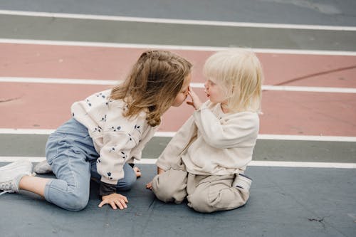 Side view of cute little boy touching nose of adorable girl while sitting on colorful sports ground together during game