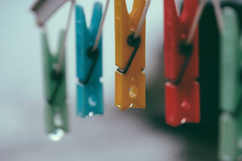 Row of plastic multicolored clothes pegs hanging on holder rope against blurred background