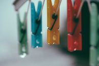 Row of plastic multicolored clothes pegs hanging on holder rope against blurred background