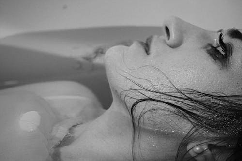 Black and white side view of unhappy young female with wet hair taking bath and thoughtfully looking away