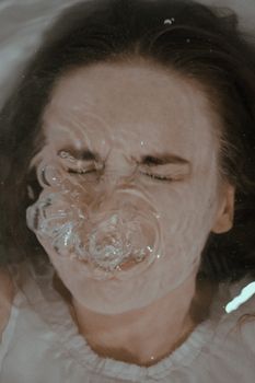 从上方看，一名闭眼浸入浴缸的女性在家中屏住呼吸，水面因此泛起气泡