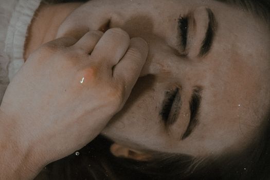 俯视视角下，一位闭眼女性躺在浴缸的水中，在浴室里屏住呼吸并捏着鼻子
