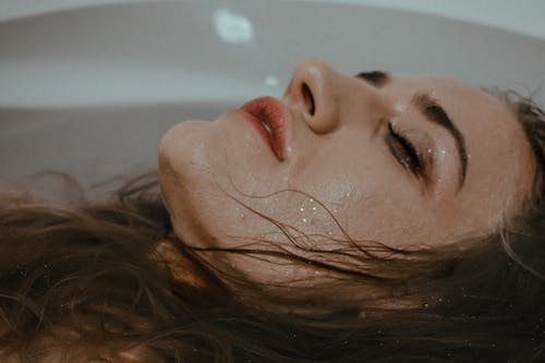 Free Relaxed female with closed eyes and smudges makeup on face lying in bathtub with hair in water at home inside Stock Photo