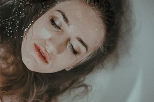 Free From above of peaceful lady with closed eyes with wet hair lying in bathtub with head resting above water inside Stock Photo