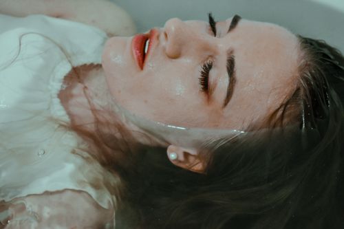 Free Relaxed female wearing white outfit lying in bathtub with closed eyes with hair immersed in water at home in bathroom Stock Photo
