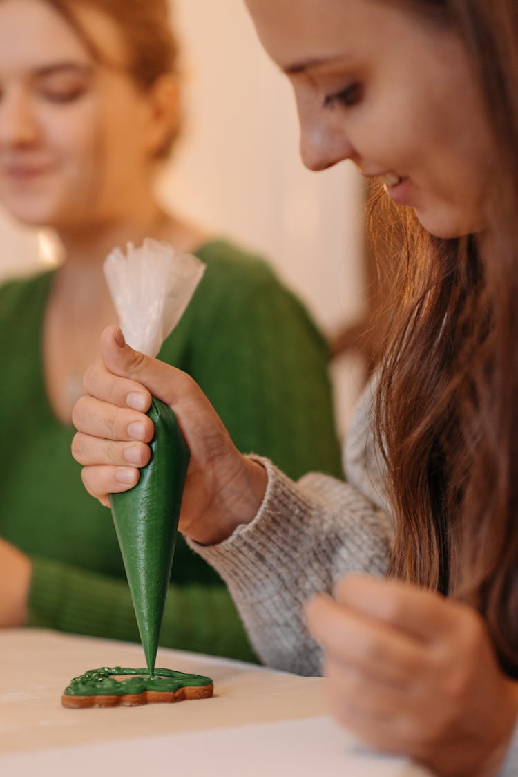 Woman In Gray Sweater Putting Green Icing On A Cookie