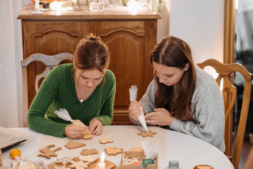 Two Young Women Putting Icing On Christmas Cookies