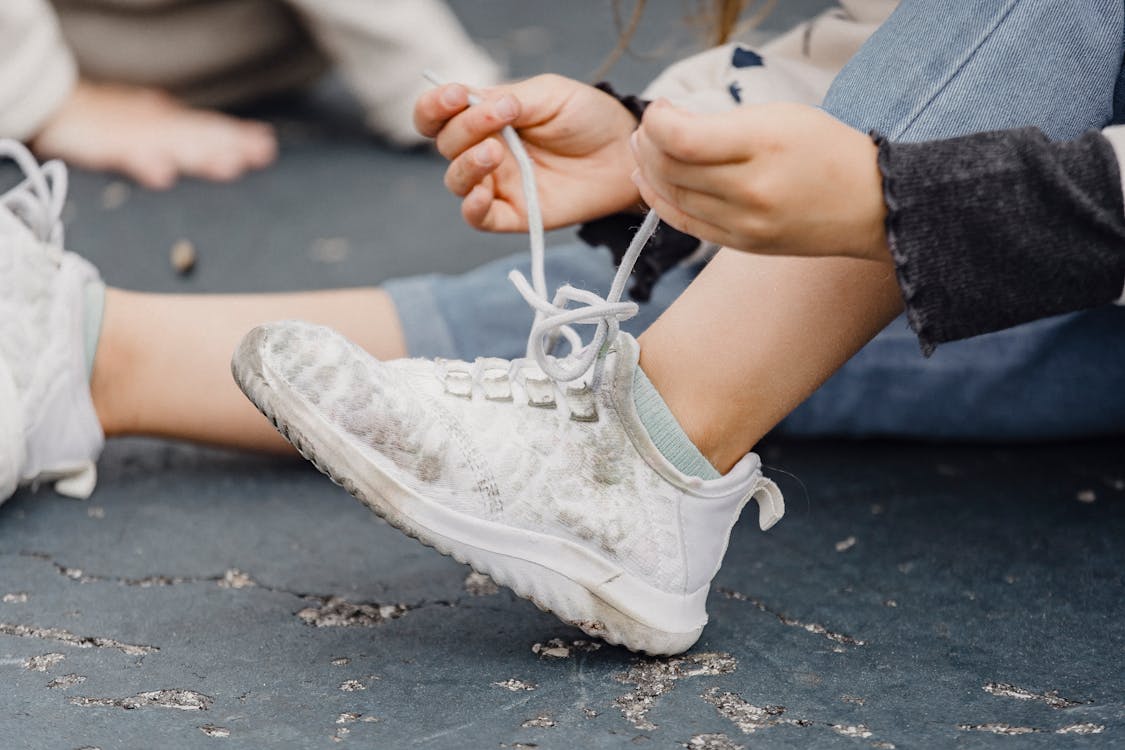 Crop kid tying shoelaces on sneakers Free Stock Photo