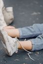 Unrecognizable kid in jeans with untied shoelaces on white dirty footwear sitting on playground with anonymous child on blurred background