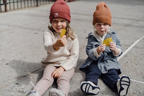 Happy siblings sitting on sidewalk with yellow leaves
