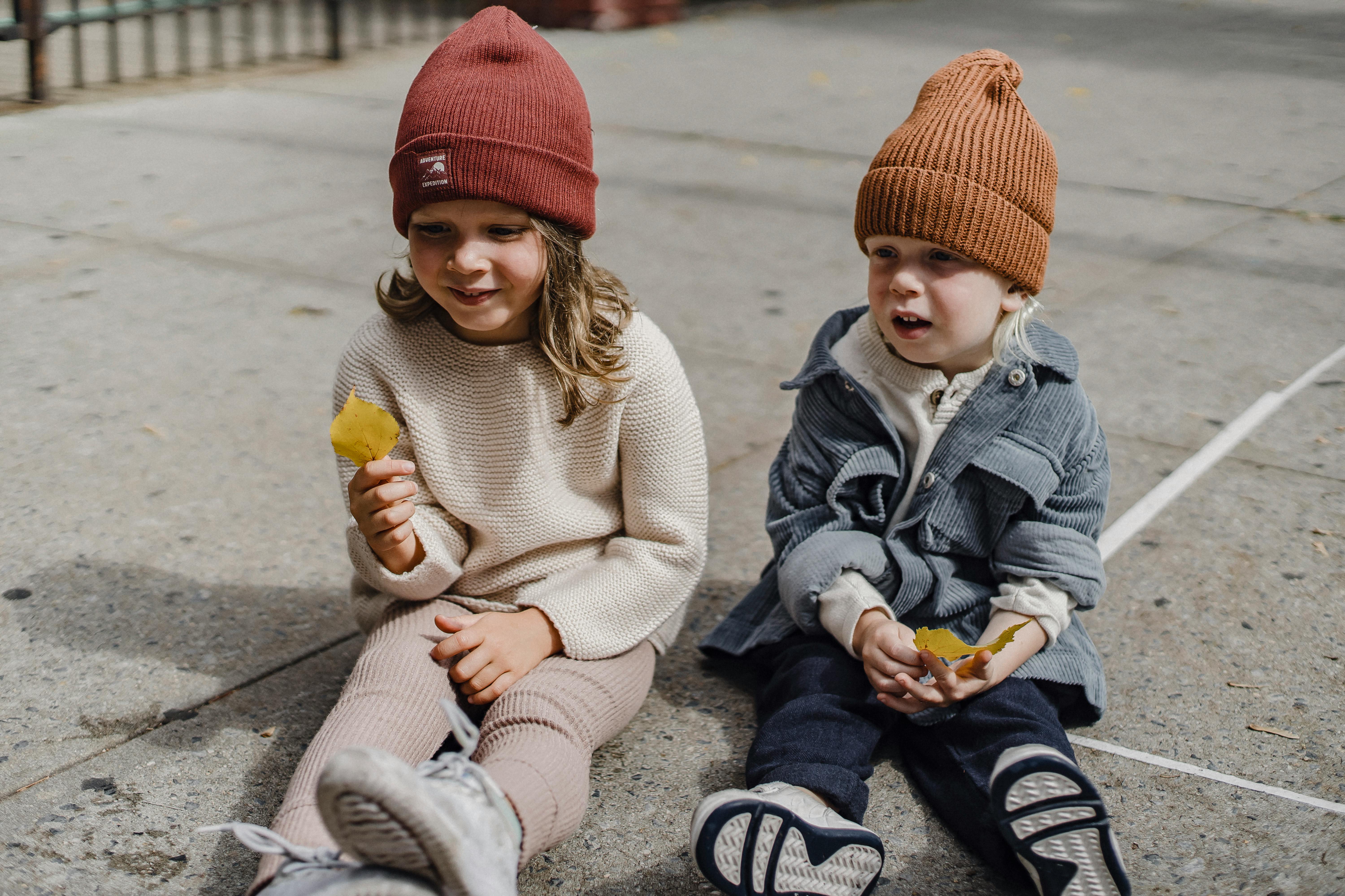 positive siblings sitting on walkway with leaves