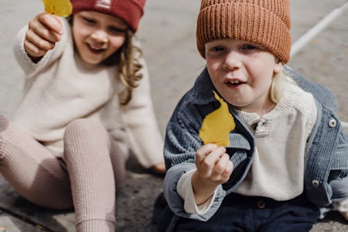 2名儿童戴着针织帽，拿着黄色和白色的蛋卷冰淇淋